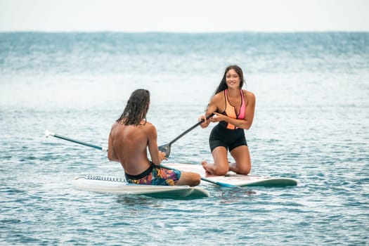 Sea woman and man on sup. Silhouette of happy young woman and man, surfing on SUP board, confident paddling through water surface. Idyllic sunset. Active lifestyle at sea or river