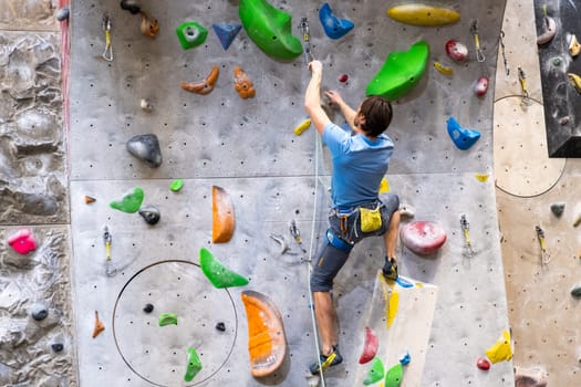 The climber trains on the artificial rock wall with insurance in bouldering gym, April 2022, Prague, Czech Republic.