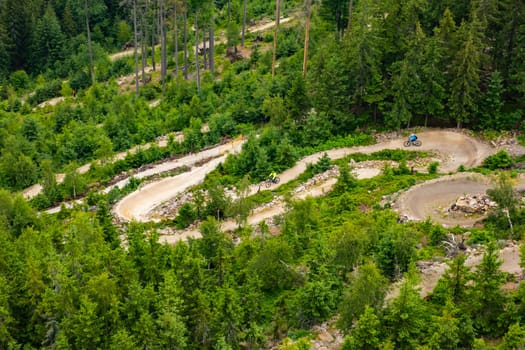 DOLNI MORAVA, CZECH REPUBLIC - MAY 14 2022: Bicyclists ride on hill slope trail park surrounded by green forests. People enjoy riding on bikes uniting with nature aerial view on May 14 in Dolni Morava