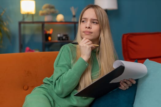 Caucasian woman freelancer work with documents on home couch, reading information, business papers prepare financial report on laptop. Young girl accountant analyzing graph documents, calculate taxes