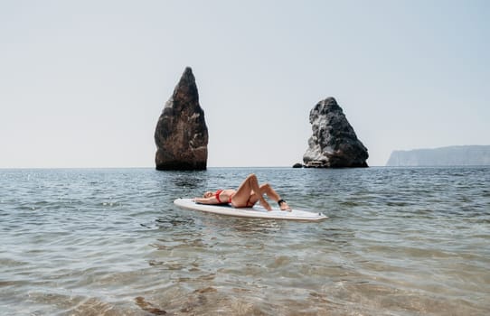 Close up shot of beautiful young caucasian woman with black hair and freckles looking at camera and smiling. Cute woman portrait in a pink bikini posing on a volcanic rock high above the sea