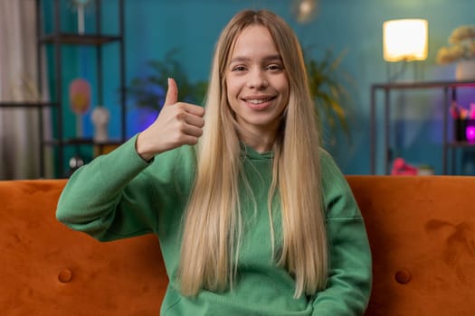 Like. Happy excited Caucasian woman looking approvingly at camera showing thumbs up, like sign positive something, good great news, positive feedback. Young girl sitting on couch at home living room