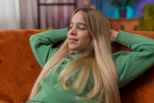 Tired young woman lying down on comfortable couch, taking a rest, daytime nap. Portrait of carefree teen girl holding hands behind head relaxing, falling asleep at home apartment living room on sofa
