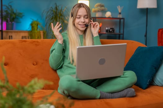 Caucasian woman wearing headset, freelance worker, call center or support service operator helpline, having talk with client or colleague communication support waving hello. Girl at home room on sofa