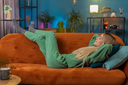 Tired young woman lying down on comfortable couch, taking a rest, daytime nap. Portrait of carefree teen girl holding hands behind head relaxing, falling asleep at home apartment living room on sofa