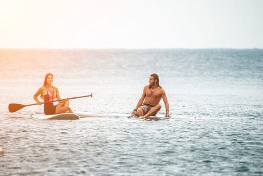 Sea woman and man on sup. Silhouette of happy young woman and man, surfing on SUP board, confident paddling through water surface. Idyllic sunset. Active lifestyle at sea or river