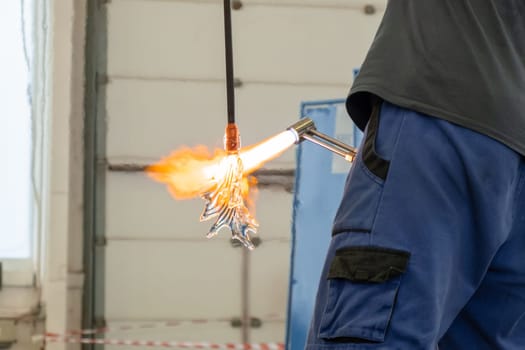 A man uses a gas burner to melt glass. A craftsman makes a glass in a leaf shaped.