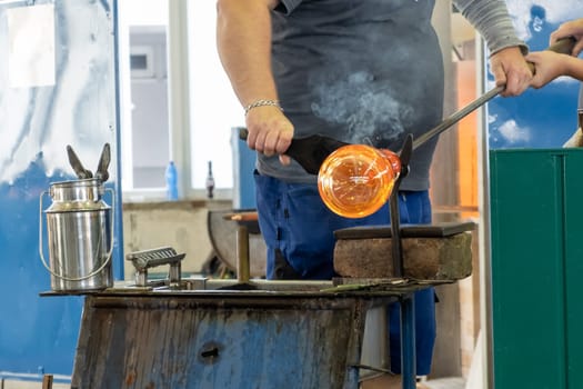 Manual glass production by glassblowing by worker at the factory.