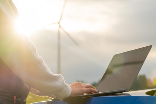 Female engineer checking the stability work of windmill with laptop in the field at sunlight. Green energy of future