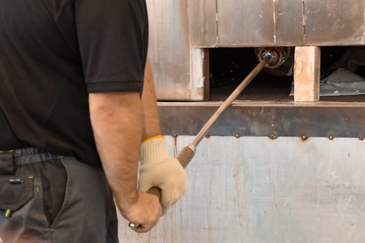 Manual glass production by glassblowing by worker at the factory. Man holding a vase in a muffle furnace.