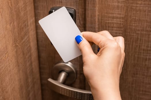 Woman hand puts key card to panel opening hotel room door. Female person with blue nails opening door