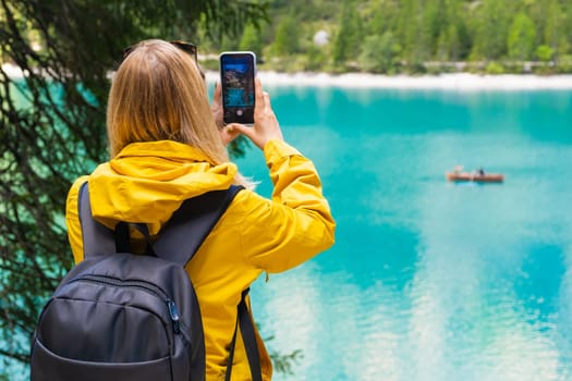 Tourist takes photo of the stunning lake Braies in the Dolomite mountains with turquoise water and wooden boats.