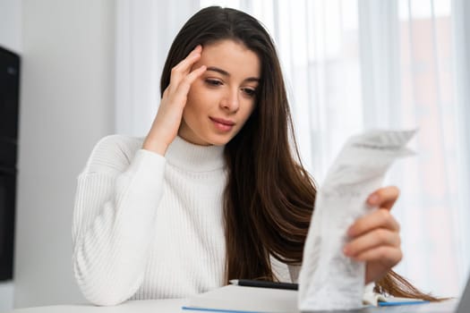 Beautiful woman holding paper bill planning finance and calculating money budget at home