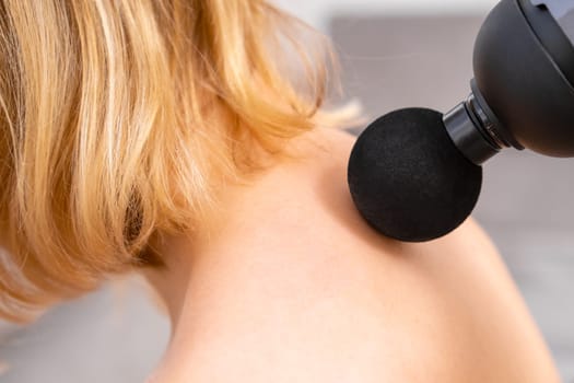Blonde hair woman massaging a neck using a massage gun. Sport recovery concept.
