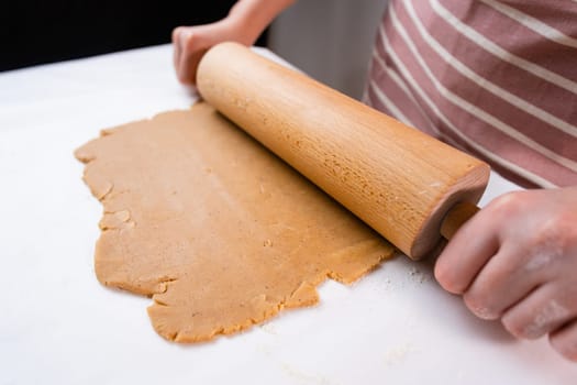 Top view of woman hands rolling out the dough with a wooden rolling pin for cookies from the shortcrust pastry.