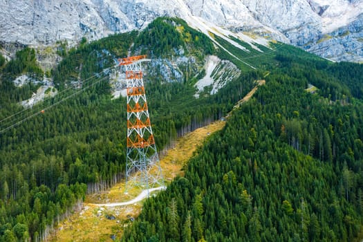 Power line pylon high in the mountains surrounded by trees, aerial view. delivery of electricity to hard to reach areas