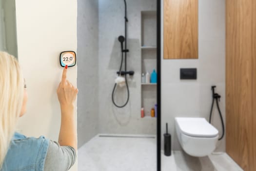 Smiling Indian woman using modern smart home system, controller on wall, positive attractive young female switching temperature on thermostat or activating security alarm in apartment