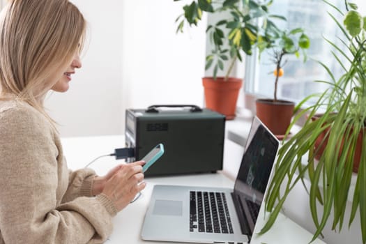 Young woman with portable power station at table in office