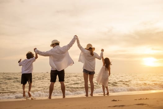 Happy Asian family have fun jumping together on beach in holiday at sunset time, Silhouette of family holding hands live healthy lifestyle on beach, back people enjoying travel and vacations concept