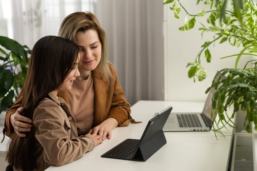 Teen child daughter studying at home in kitchen with mom. Teenage school kid girl distance learning virtual online class with mother or tutor helping doing homework together during remote education.