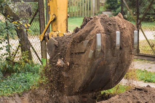 Excavation work on the construction site. A bucket of a bulldozer digs the ground with a grass close-up in an industrial area.