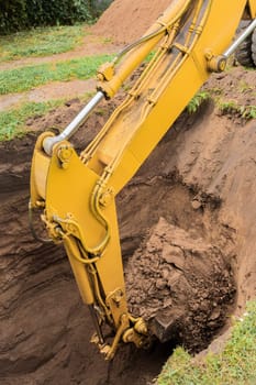 The hydraulic piston of the excavator bucket with the ground digs a hole on the construction site close-up.