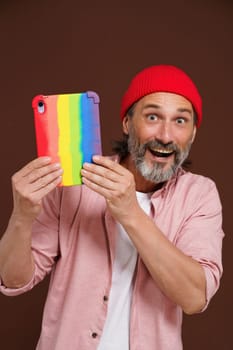 Coming out LGBTQ concept. Happy European man smiling while holding tablet PC in colorful rainbow case. Modern man with digital device represents LGBTQ community. High quality photo