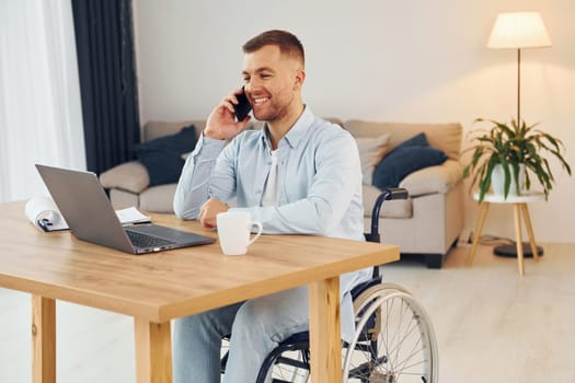 Laptop on the table. Disabled man in wheelchair is at home.