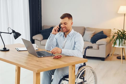 Using laptop. Disabled man in wheelchair is at home.