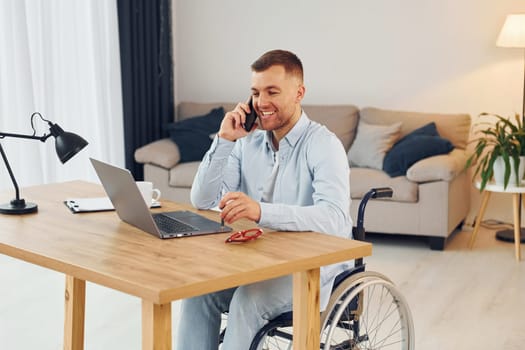 Using laptop. Disabled man in wheelchair is at home.