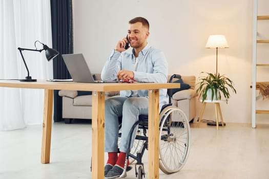 Using laptop. Disabled man in wheelchair is at home.