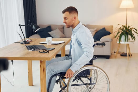 Working by using laptop. Disabled man in wheelchair is at home.
