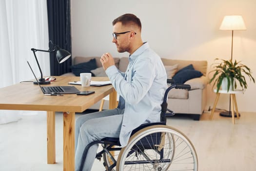 Working by using laptop. Disabled man in wheelchair is at home.