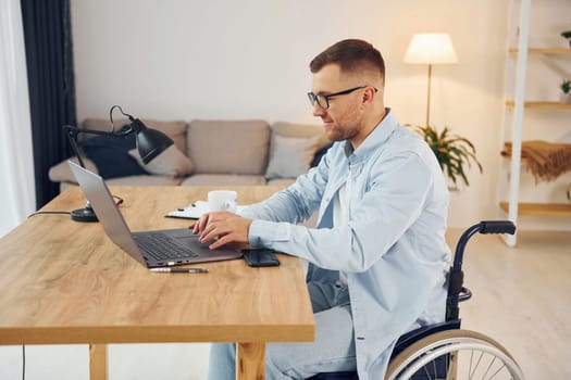 Working by using laptop. Disabled man in wheelchair is at home.