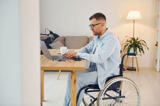 Working by using laptop. Disabled man in wheelchair is at home.