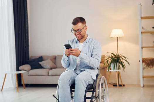 Using phone. Disabled man in wheelchair is at home.