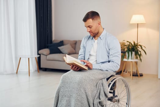 Reading book. Disabled man in wheelchair is at home.