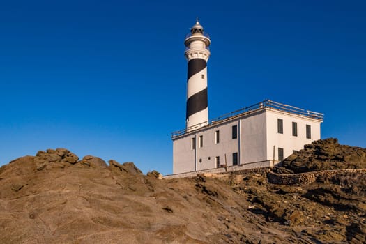 The lonely and spiral black and white painted lighthouse Far de Favaritx in the east of the island of Menorca, Balearic Islands, Spain