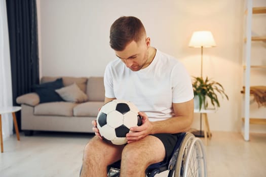 With soccer ball. Disabled man in wheelchair is at home.
