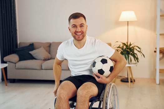 Soccer fan with ball. Disabled man in wheelchair is at home.