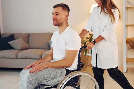 Woman is helping. Disabled man in wheelchair is at home.