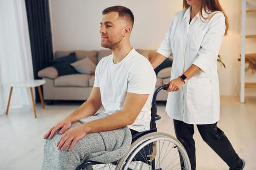 Woman is helping. Disabled man in wheelchair is at home.