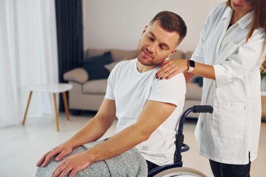 Woman is helping. Disabled man in wheelchair is at home.