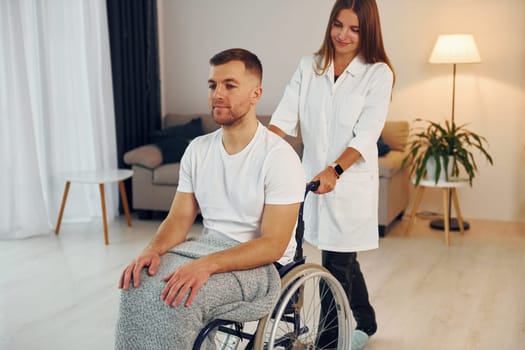 Medical worker. Woman is helping. Disabled man in wheelchair is at home.