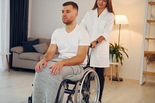 Medical worker. Woman is helping. Disabled man in wheelchair is at home.