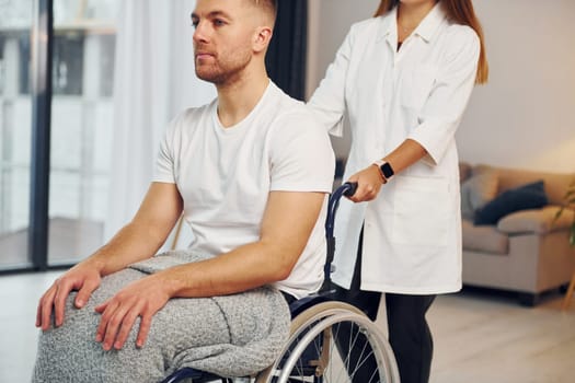 Medical worker. Woman is helping. Disabled man in wheelchair is at home.