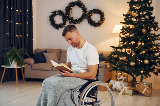 Reading the book. New year is coming. Disabled man in wheelchair is at home.