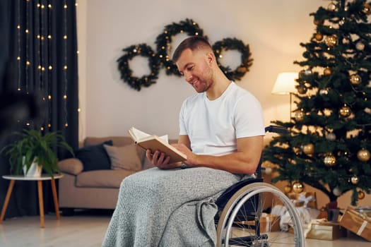 Reading the book. New year is coming. Disabled man in wheelchair is at home.