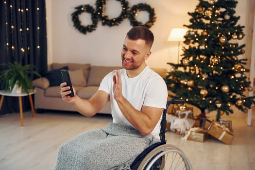 Using smartphone to communicate with people. New year is coming. Disabled man in wheelchair is at home.