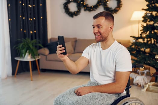 Using smartphone to communicate with people. New year is coming. Disabled man in wheelchair is at home.